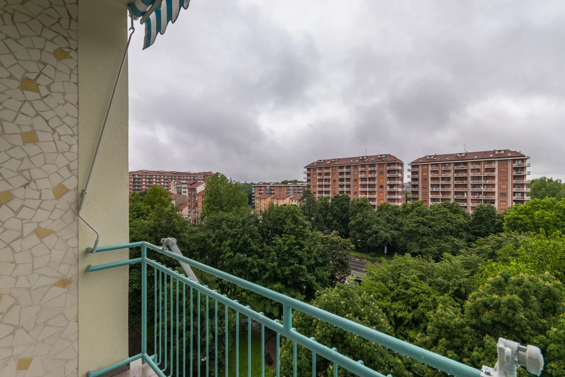 Un balcón ofrece vistas de árboles frondosos y edificios de apartamentos bajo un cielo nublado.