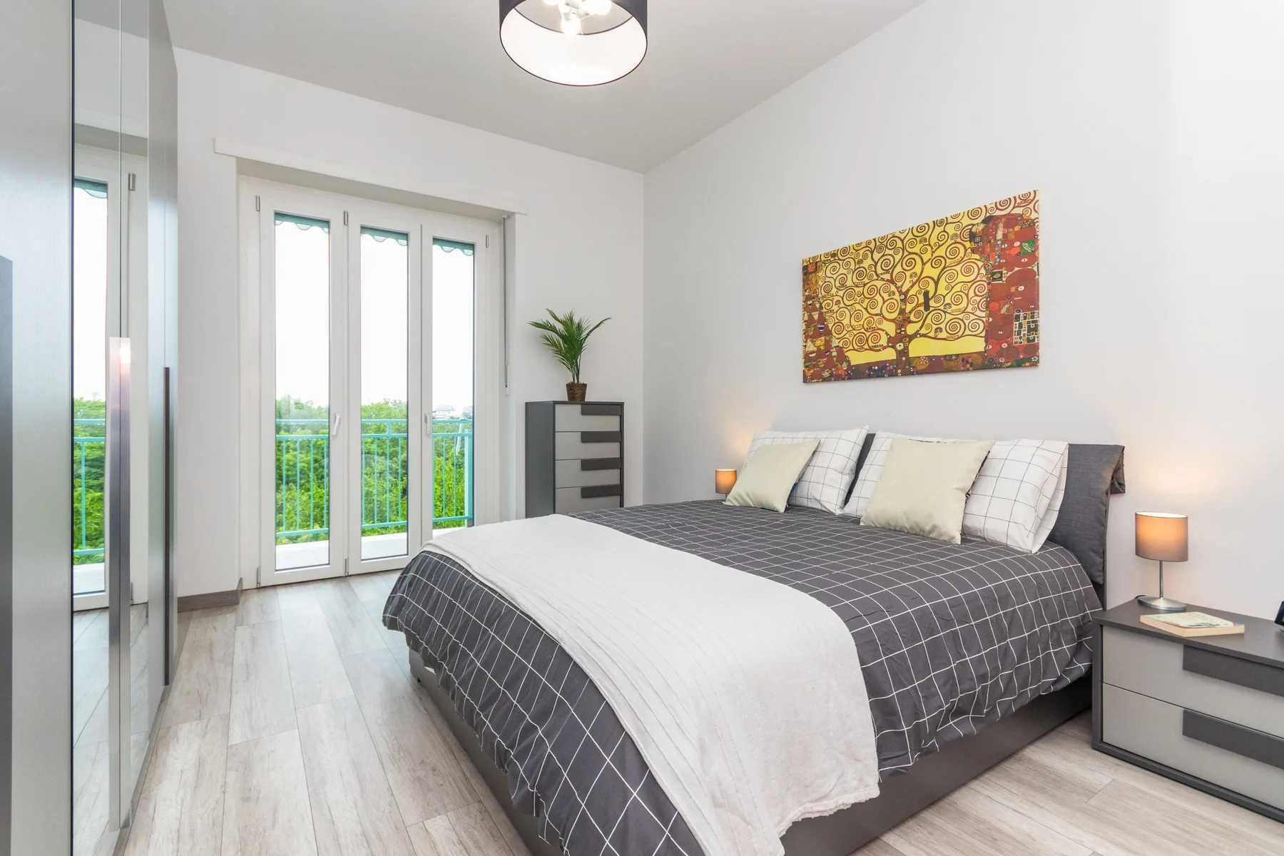A bright bedroom with a large bed, balcony doors, and colorful wall art.