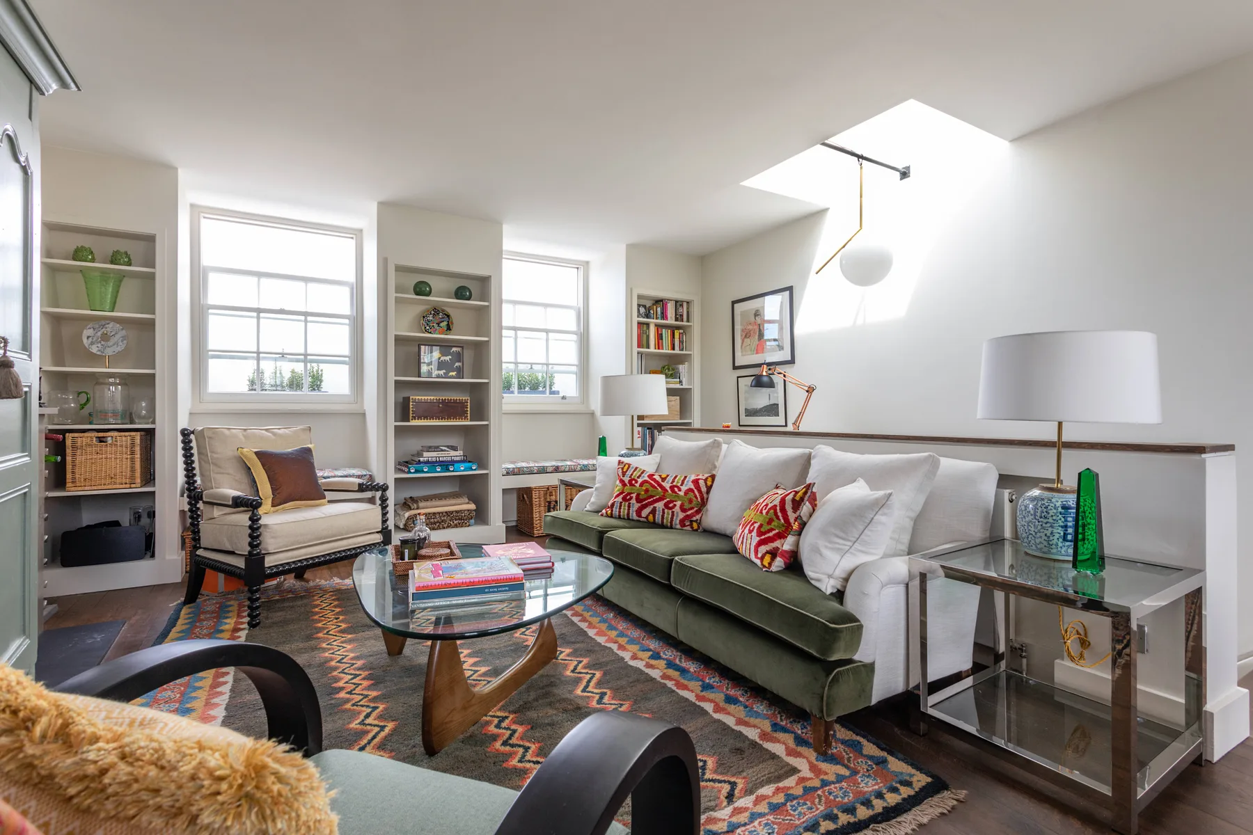 A bright living room with seating, colorful cushions, and a patterned rug.