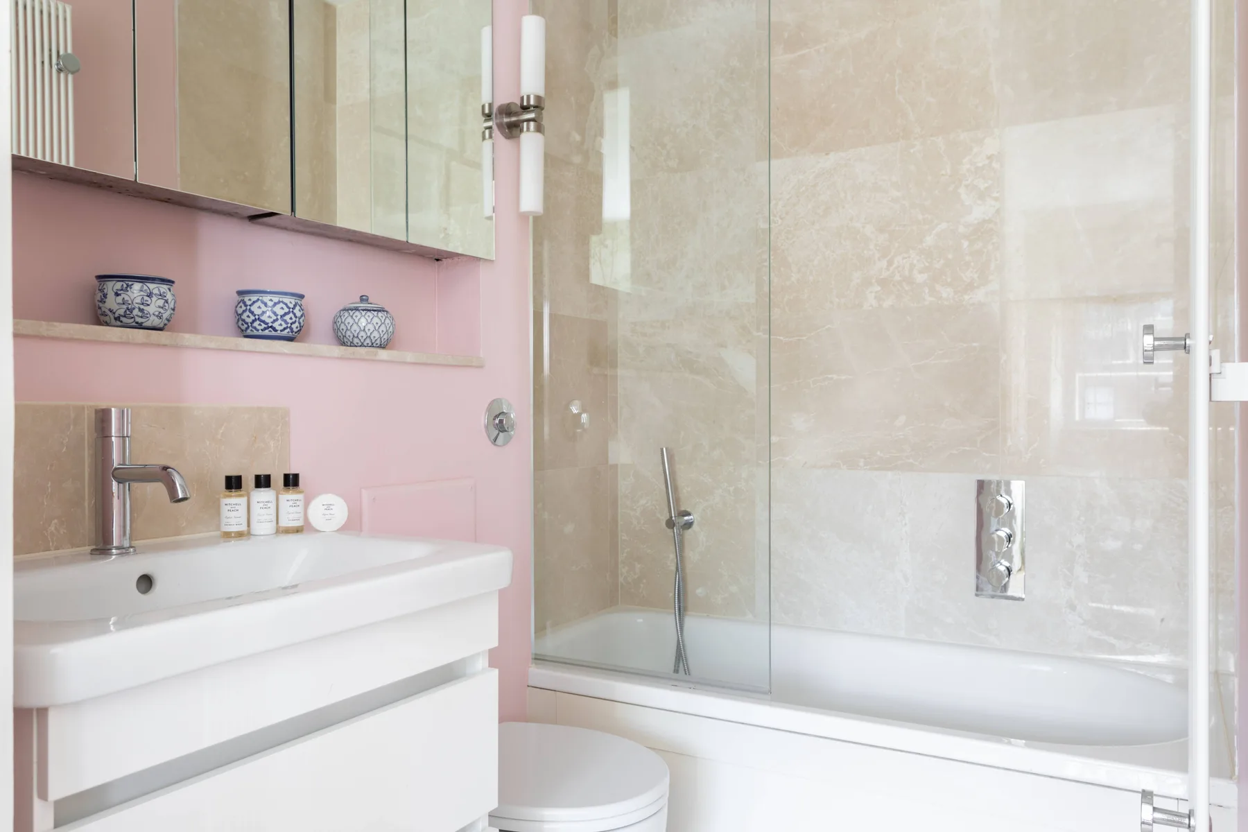 A bathroom with a sink, toilet, and bathtub behind a glass shower screen.