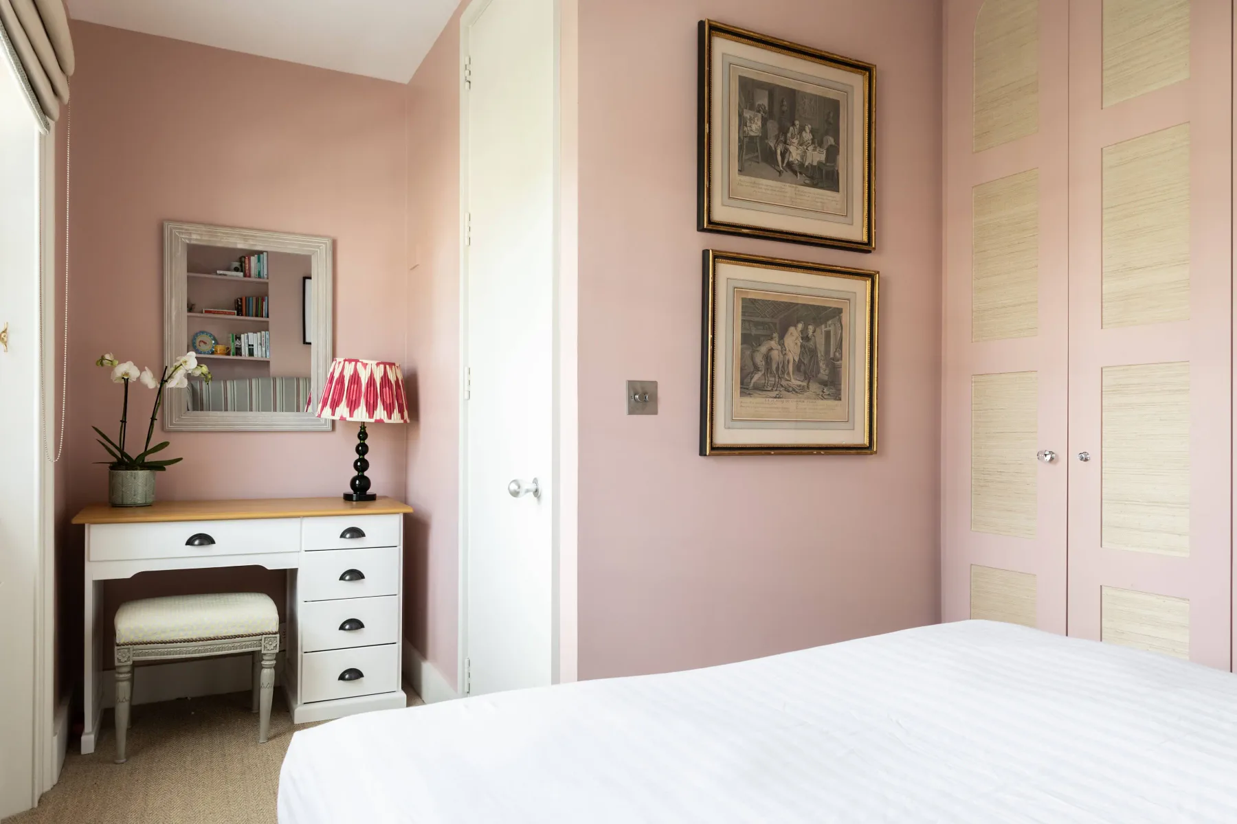 A bedroom with a white bed and pink walls.