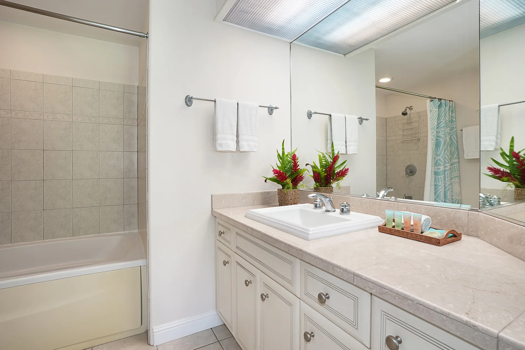 A bright bathroom with a long vanity, sink, and bathtub.
