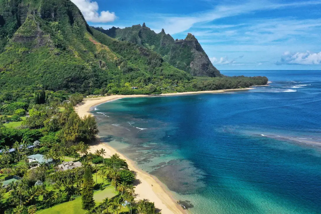 A tropical coastline curves beneath a lush green mountain range.