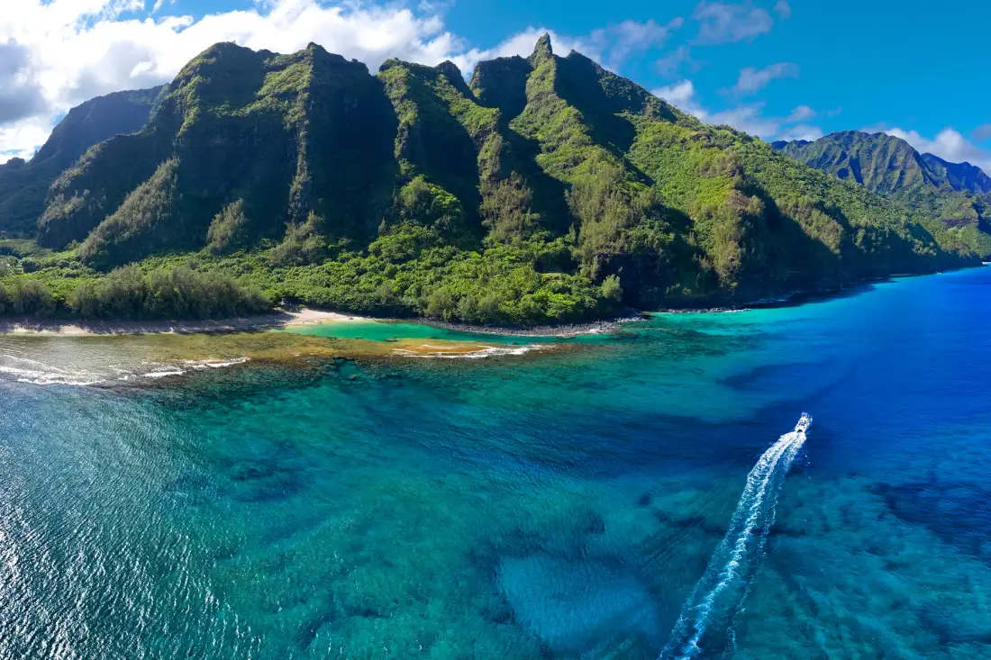 Aerial view of a lush mountain coastline beside clear turquoise water.