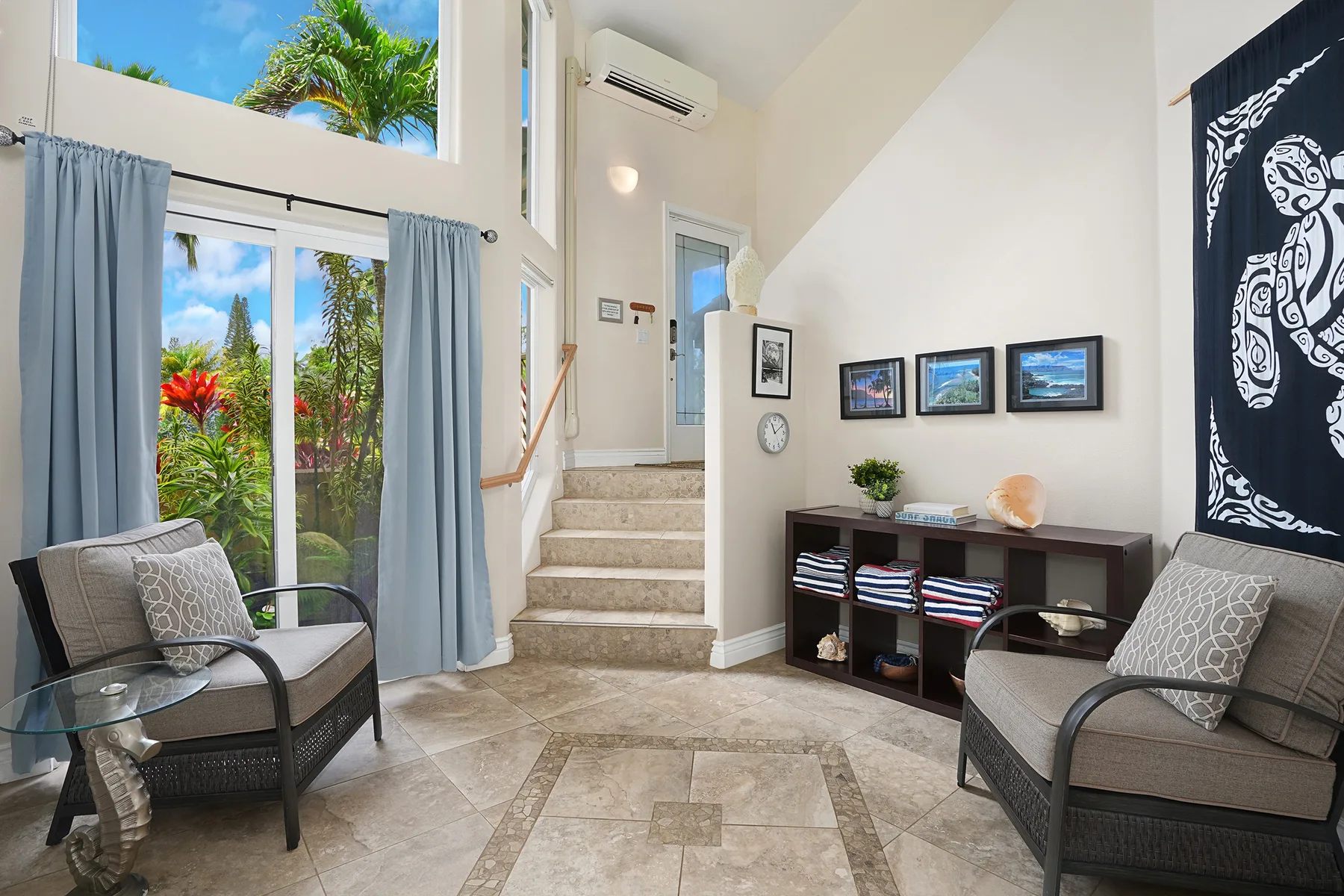 A bright living room with seating, a staircase, and large windows overlooking greenery.