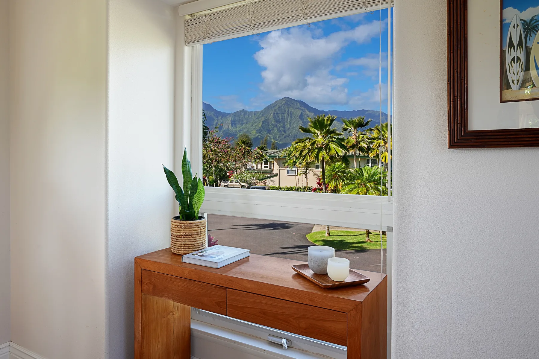 A wooden console table sits beside a large window overlooking palm trees and mountains.