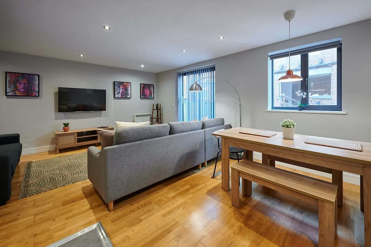 Una sala de estar con asientos grises, un televisor y una mesa de comedor de madera.