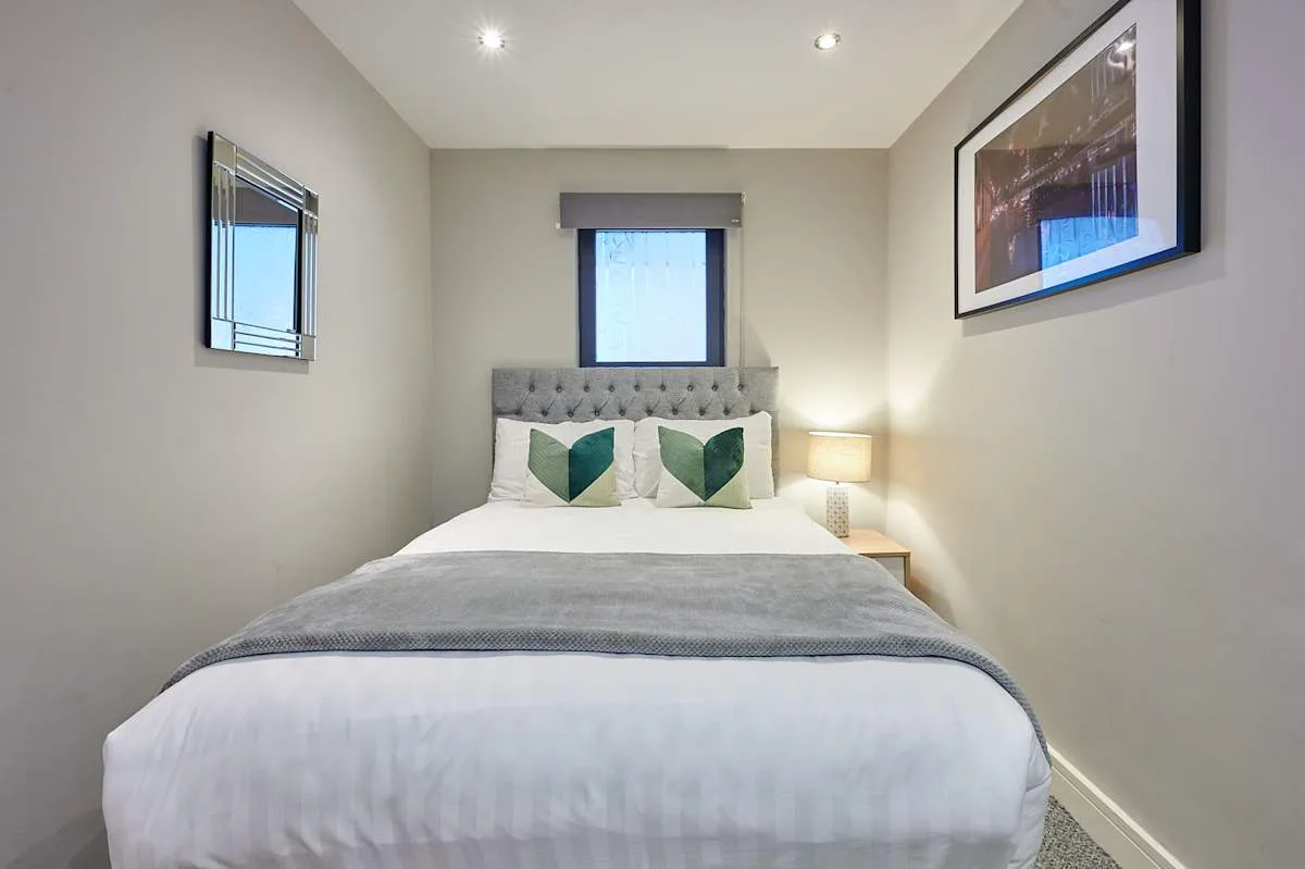 Dormitorio con una cama bien tendida, cojines decorativos verdes y cuadros en la pared.