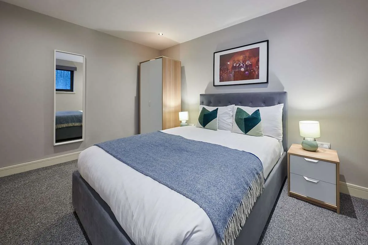 Un dormitorio con una cama bien tendida, cojines verde azulado y lámparas de mesilla a juego.