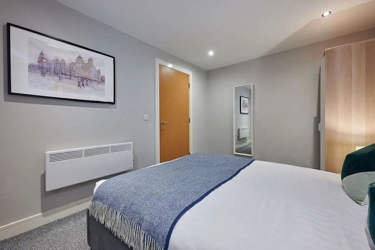 Un dormitorio con la cama arreglada, una lámina enmarcada y un armario con espejo.