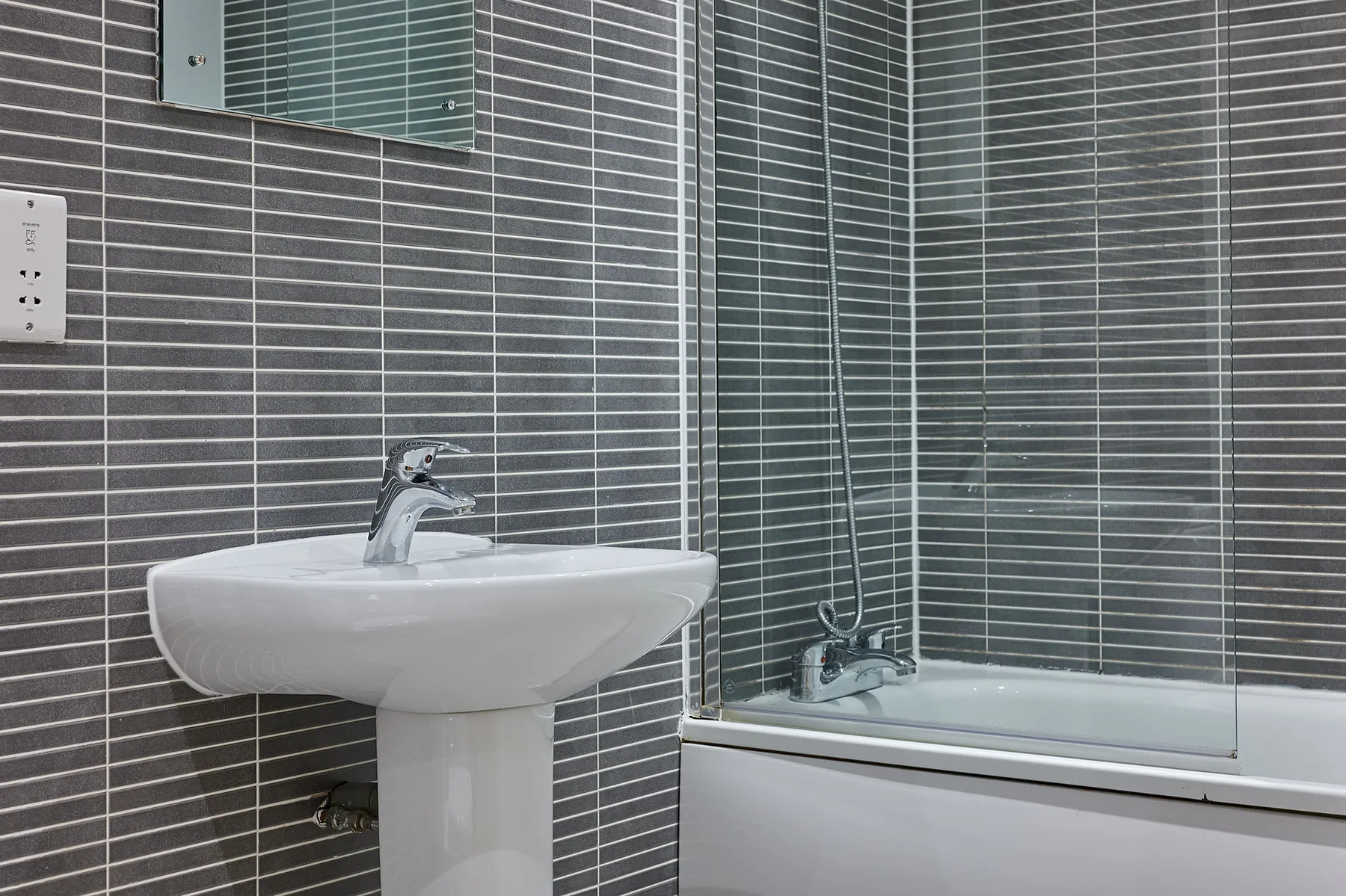 Un baño con azulejos, un lavabo con pedestal y una ducha de vidrio.