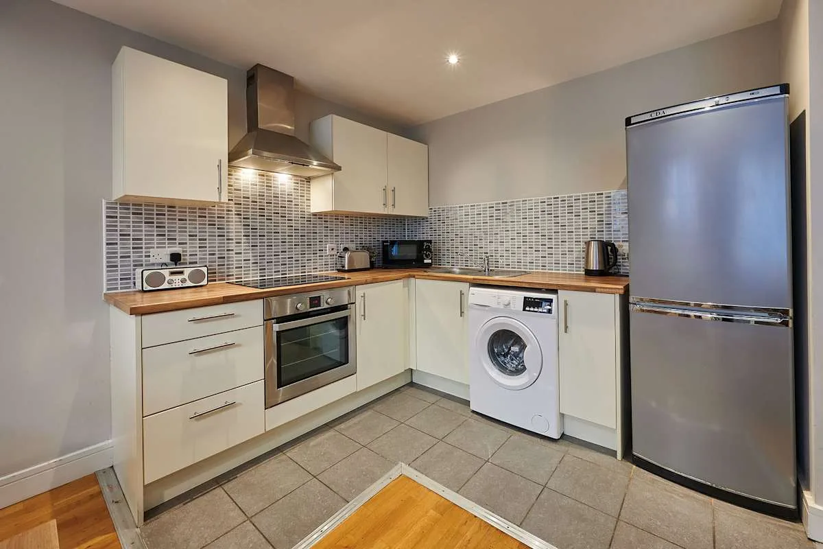 Una cocina equipada con gabinetes claros, un salpicadero de azulejos y una lavadora.