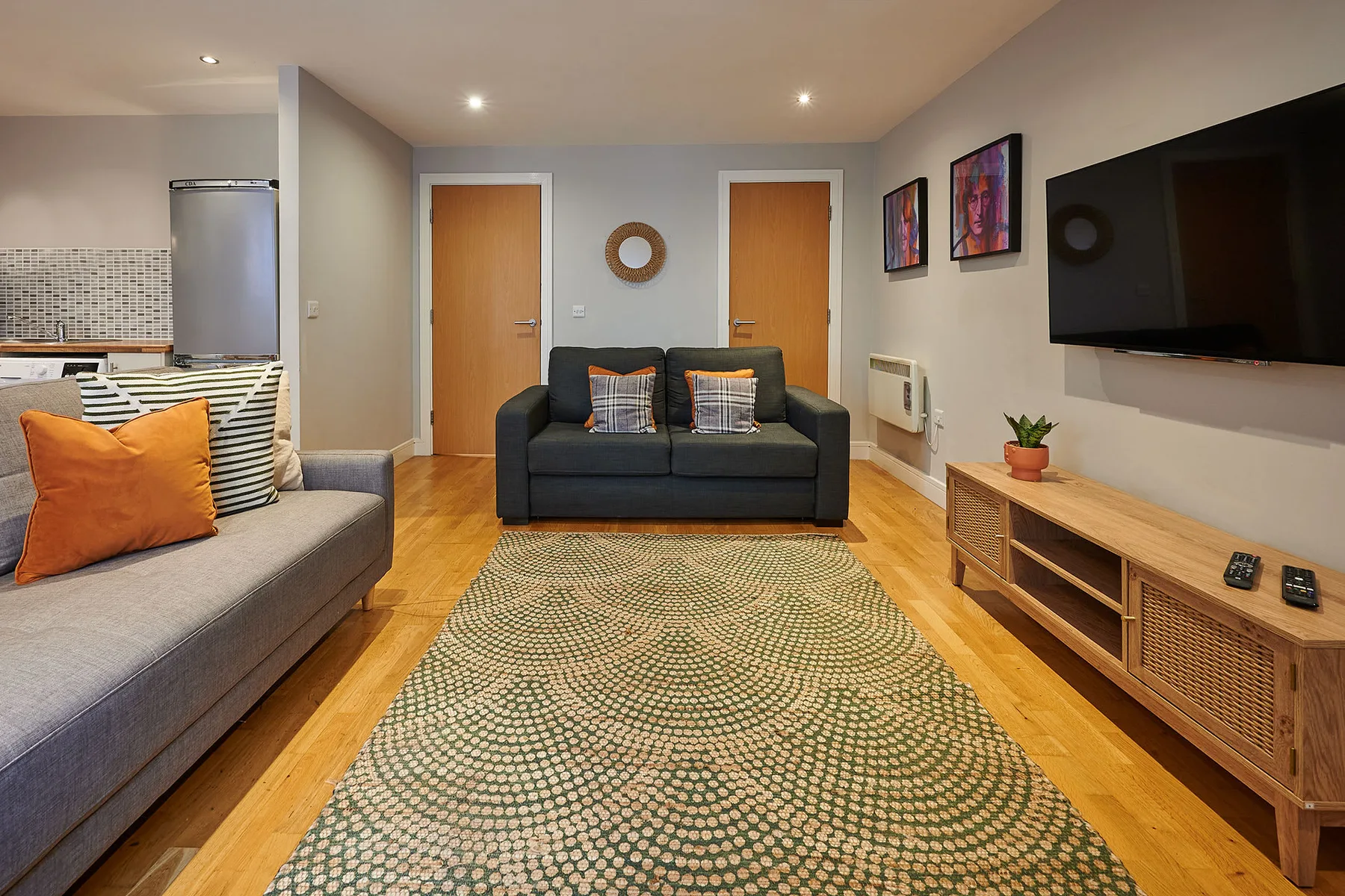Una sala de estar con sofás, una alfombra y un televisor en la pared.