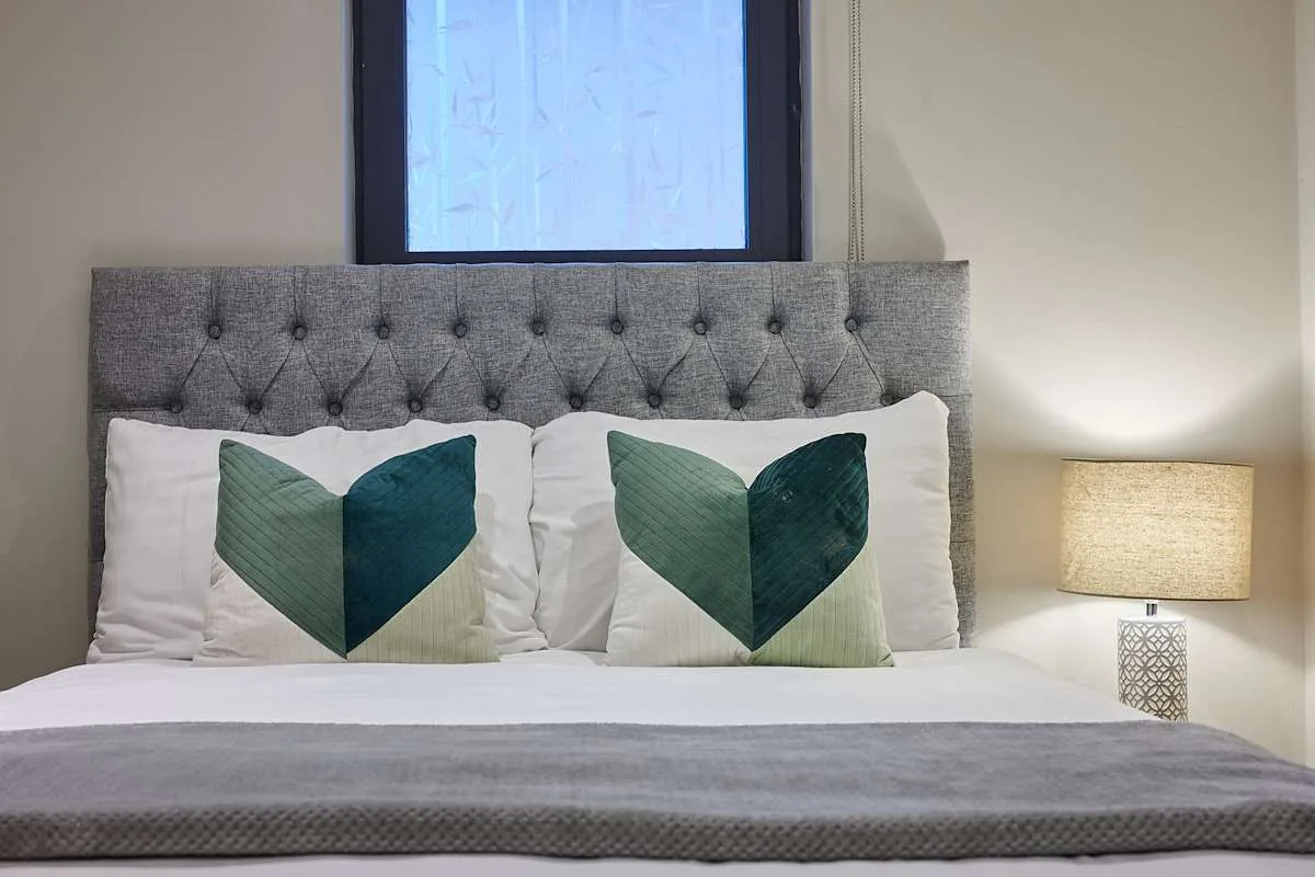 Un dormitorio con una cama tendida y cojines decorativos verdes.