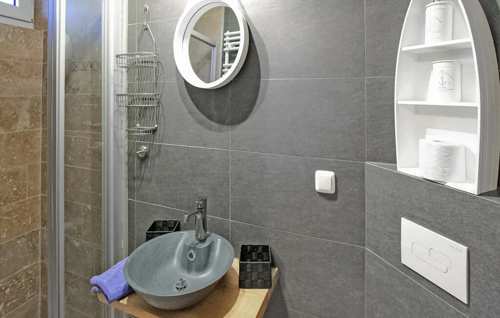 Un lavabo de baño con azulejos, espejo redondo y estantes en la pared.