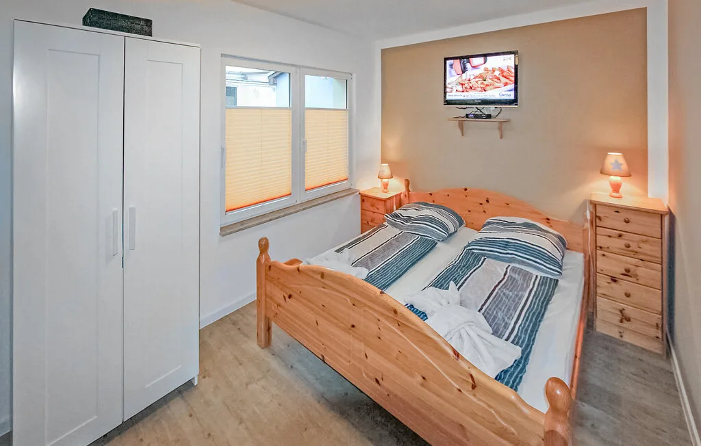 Un dormitorio con una cama de madera, ropa de cama a rayas y un televisor en la pared.