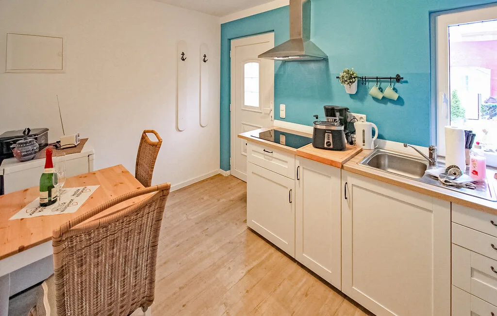 Una cocina luminosa con gabinetes blancos, un fregadero en la encimera y una pequeña mesa de comedor.