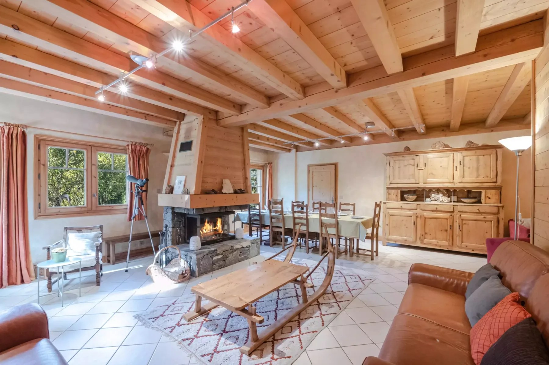 A rustic living and dining area features a stone fireplace and wooden ceiling beams.