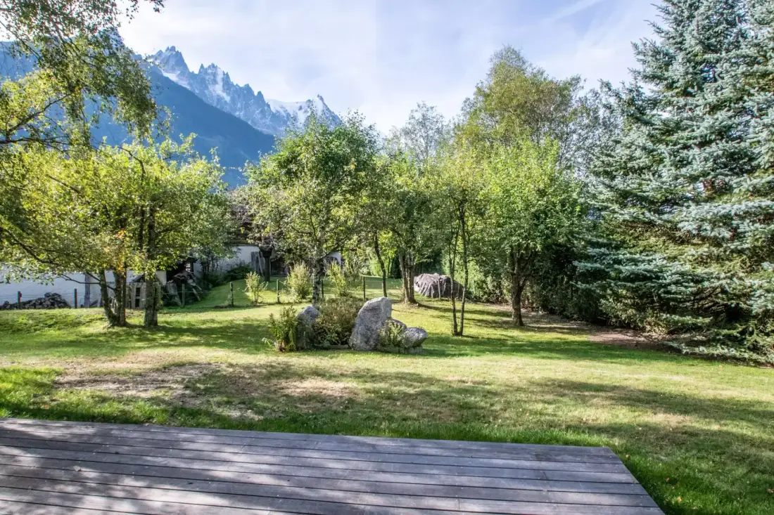 A landscaped garden with trees, boulders, and mountain peaks in the background.