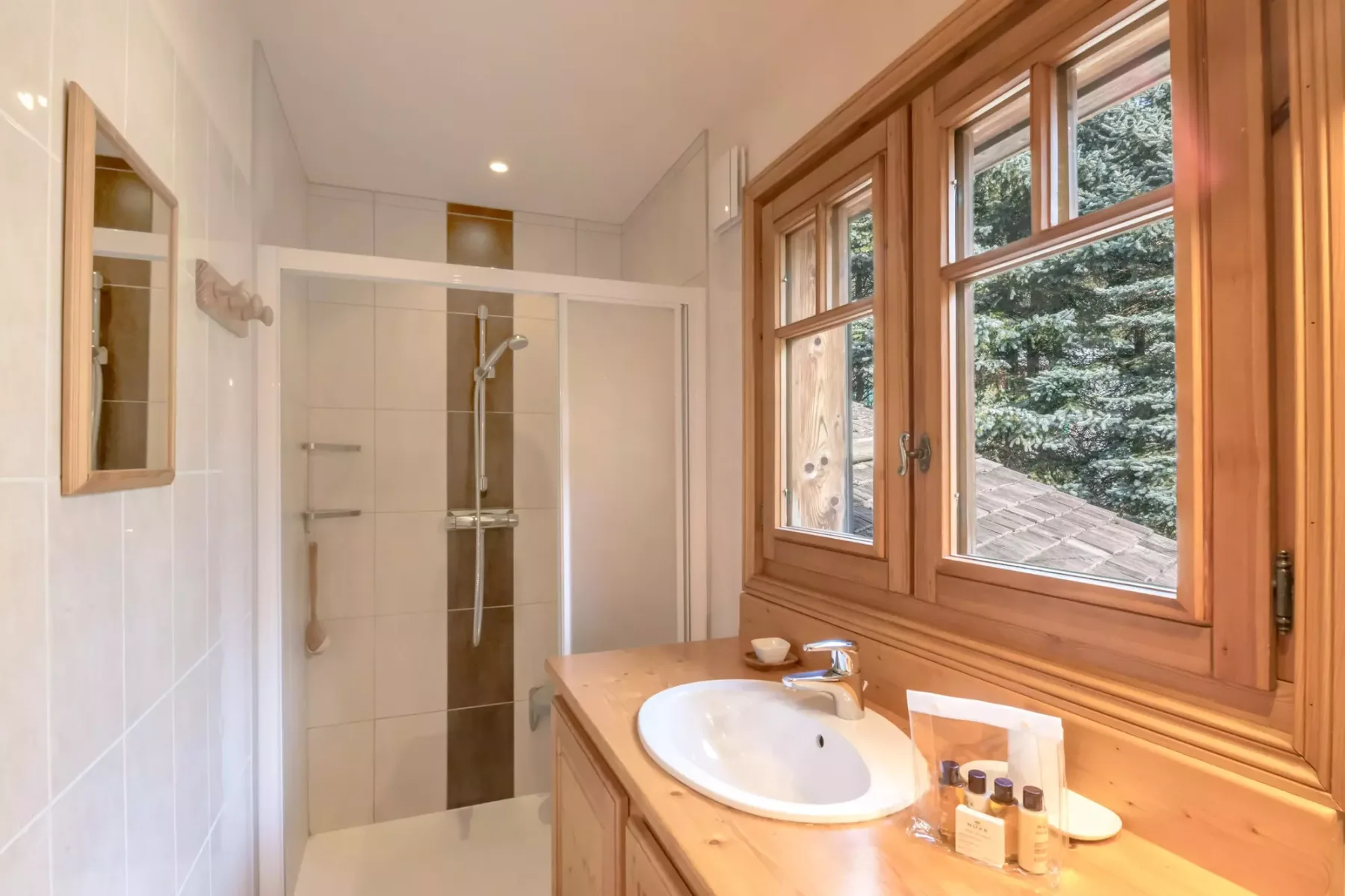 A bright bathroom with a shower, sink, and large wood-framed windows.