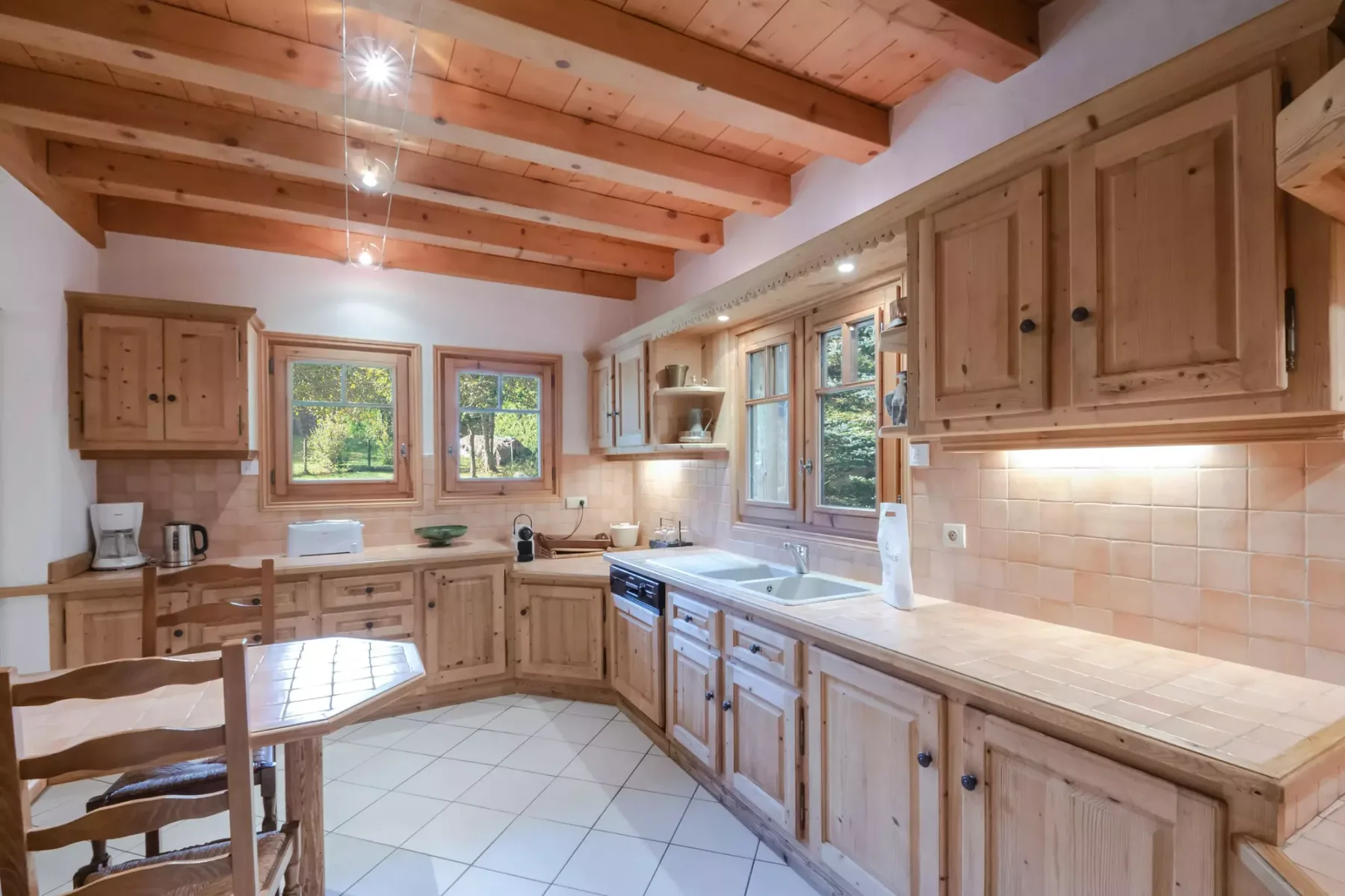 A spacious kitchen with wooden cabinets, tiled flooring, and windows overlooking greenery.