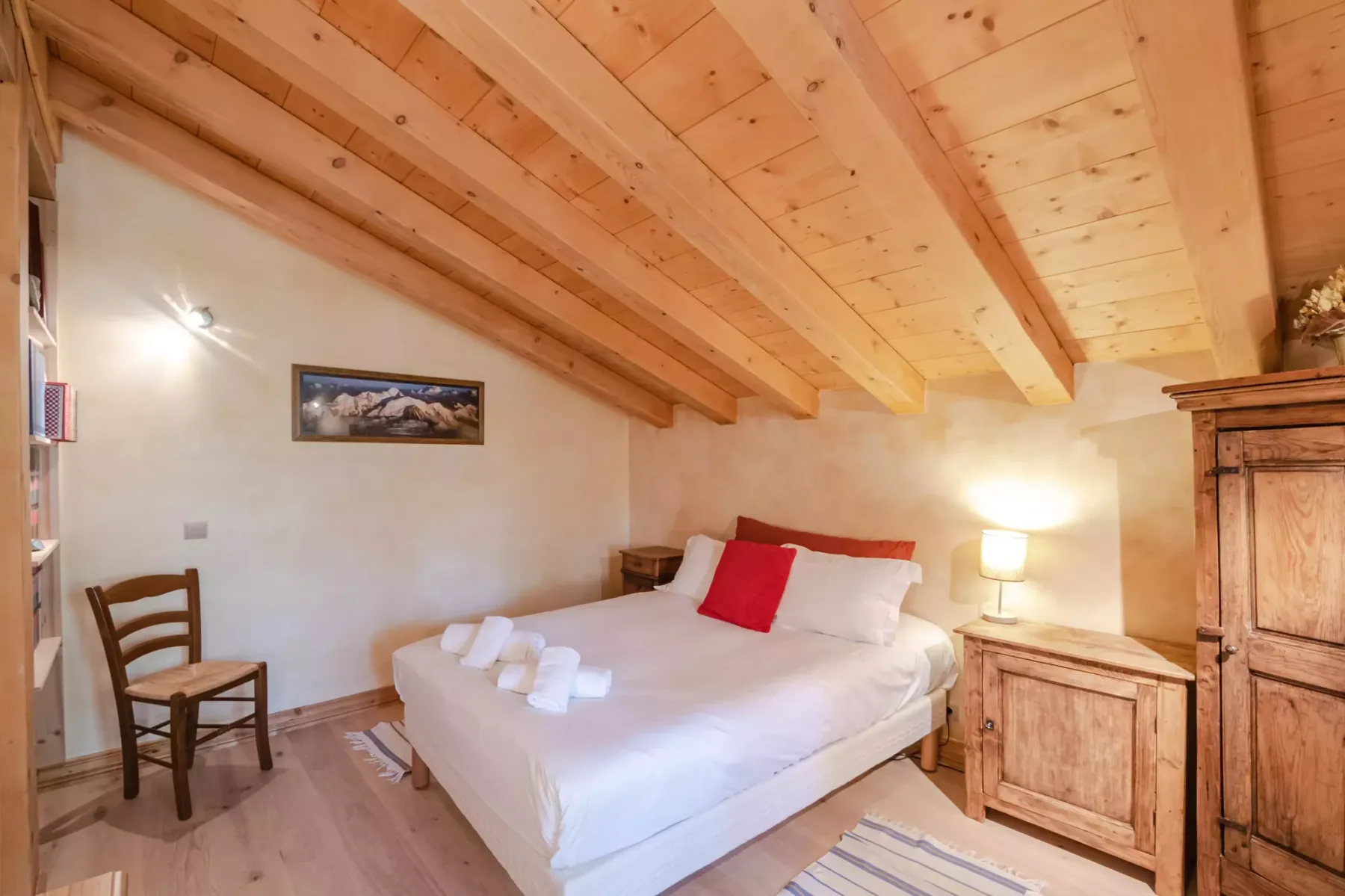 A bedroom with a white bed beneath a sloped wooden ceiling.