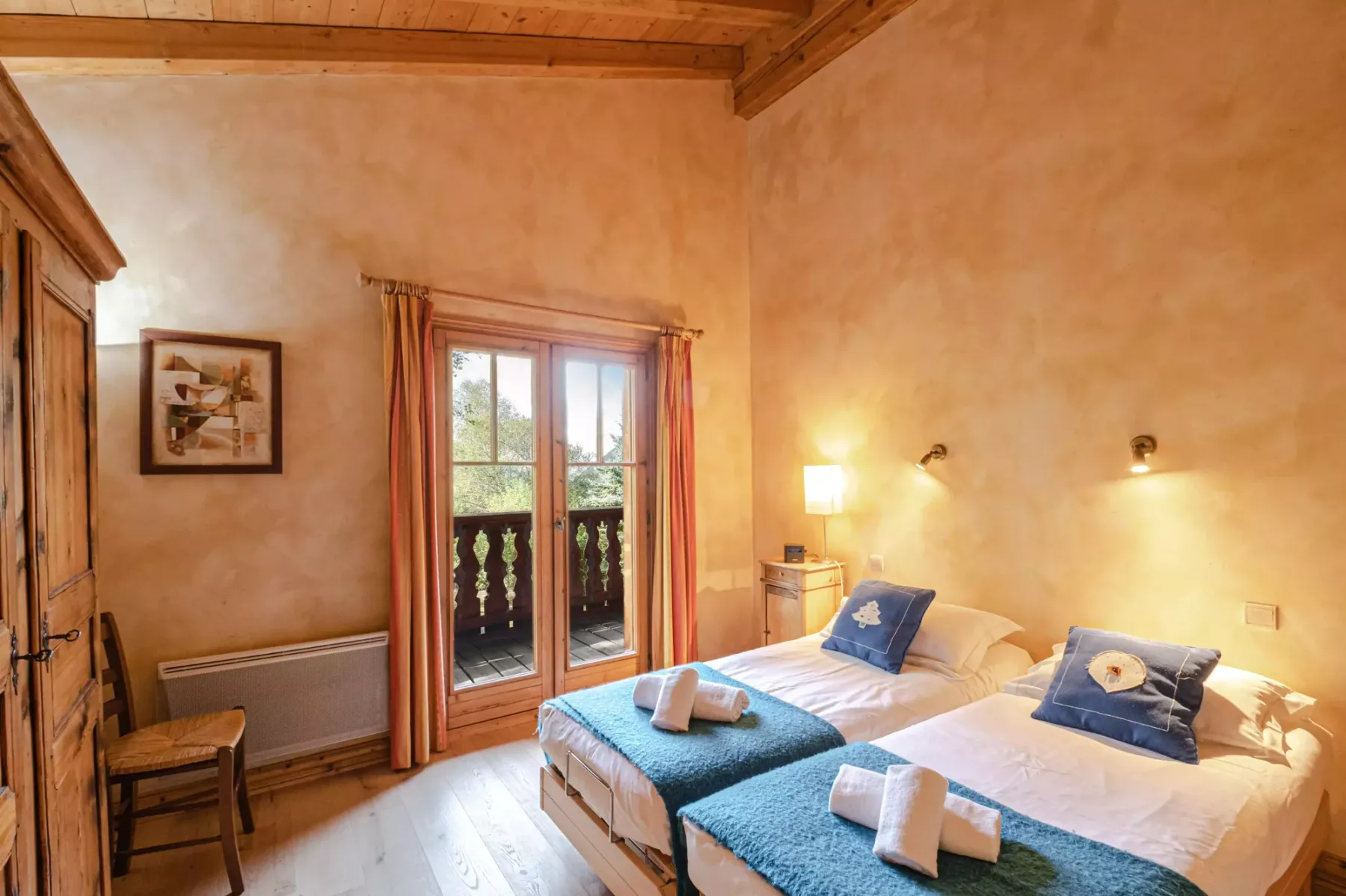 A bedroom with two beds, blue bed runners, and a glass door opening to a balcony.