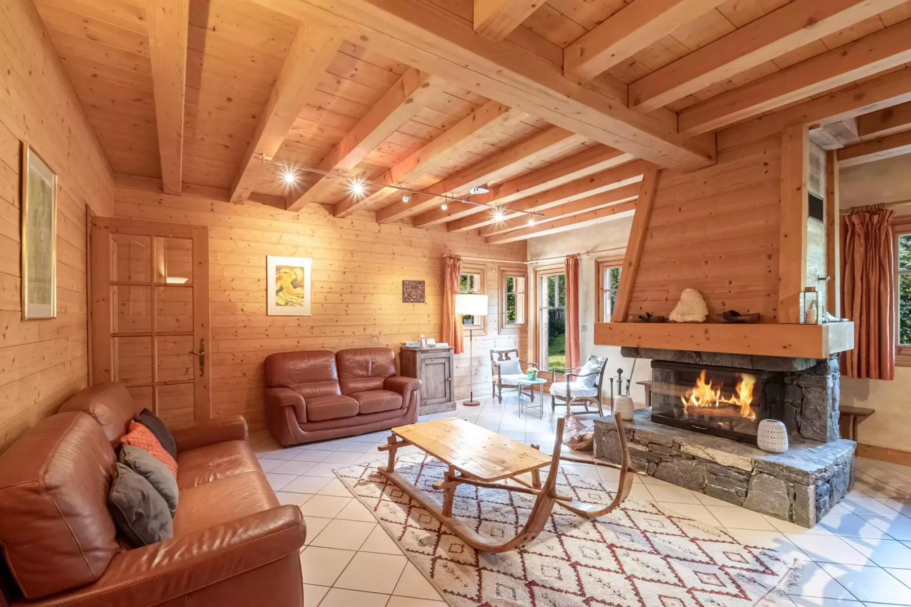 A timber-paneled living room has leather seating, a coffee table, and a lit fireplace.