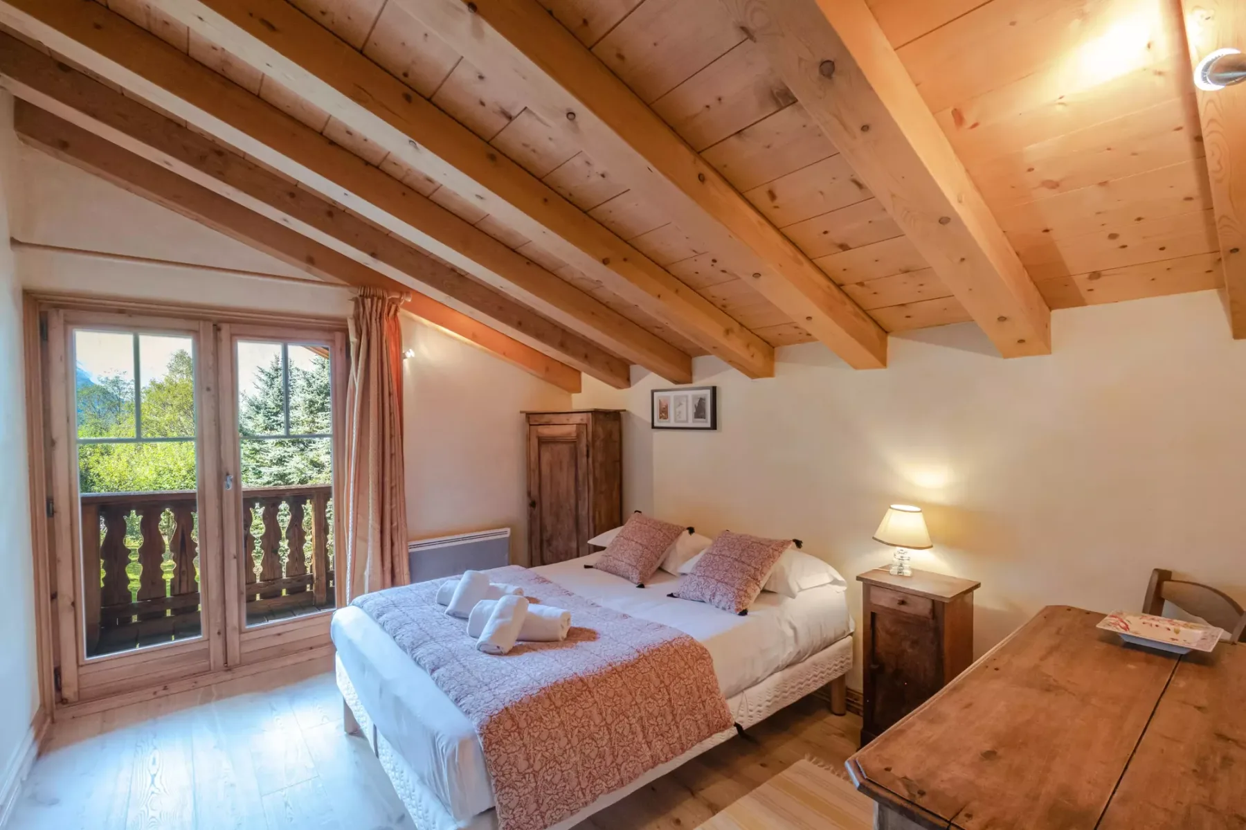 A bedroom with a bed beneath a sloped wooden ceiling and doors opening onto a balcony.
