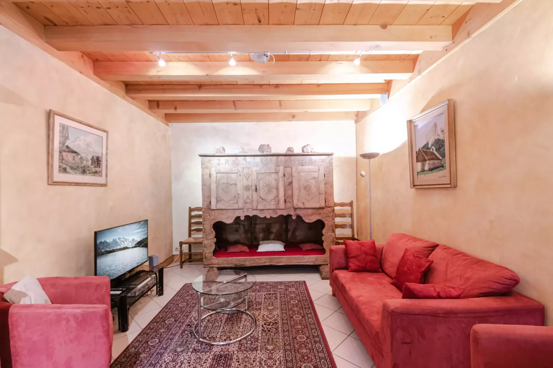 A living room with red seating, a patterned rug, and a television.