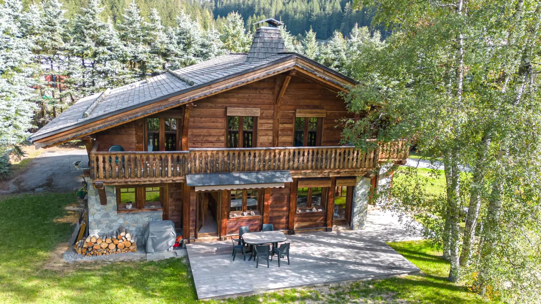A wooden cabin with a balcony and outdoor seating on a sunny patio.