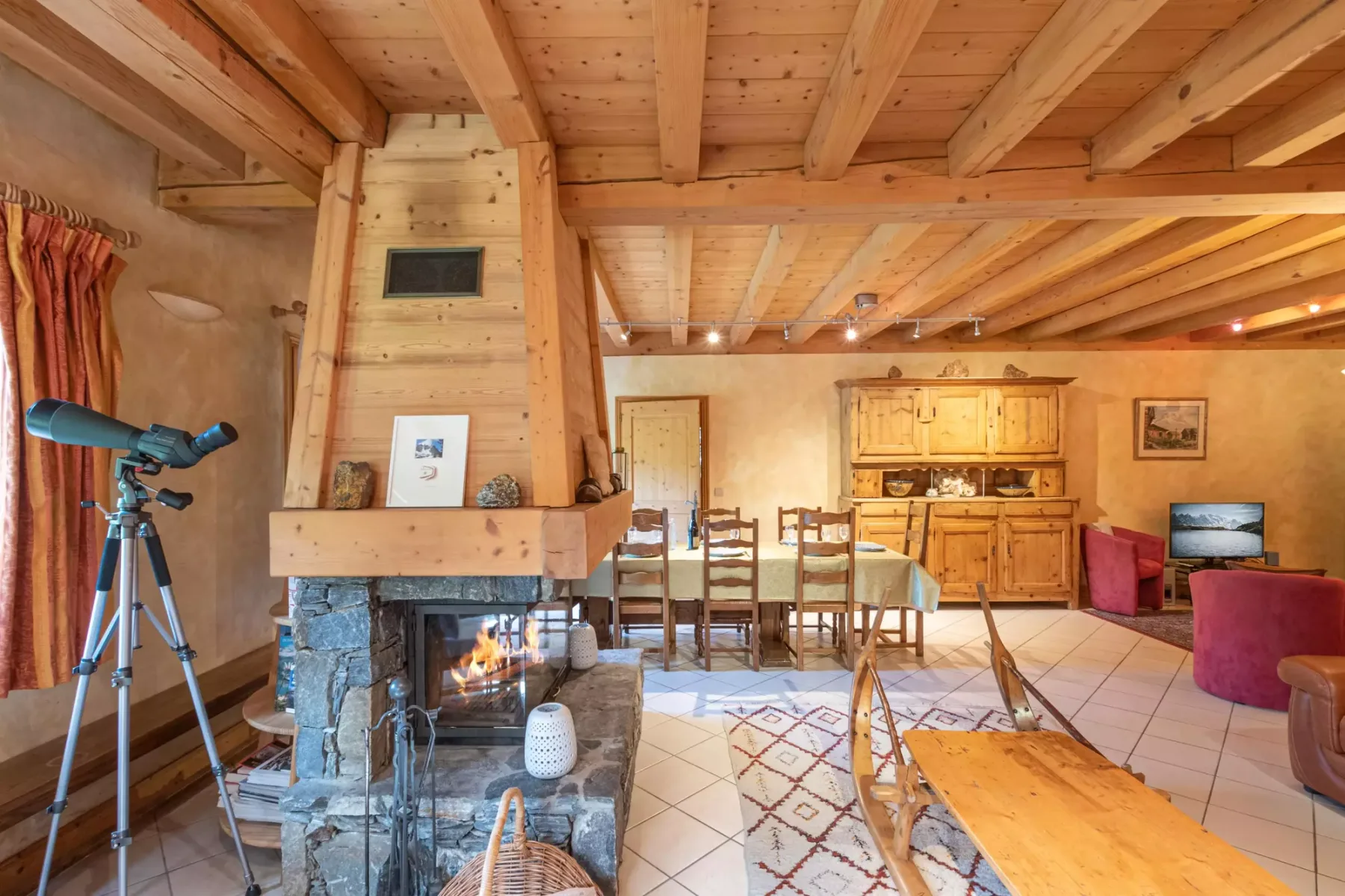 A timber-beamed living and dining room with a stone fireplace and wooden furniture.
