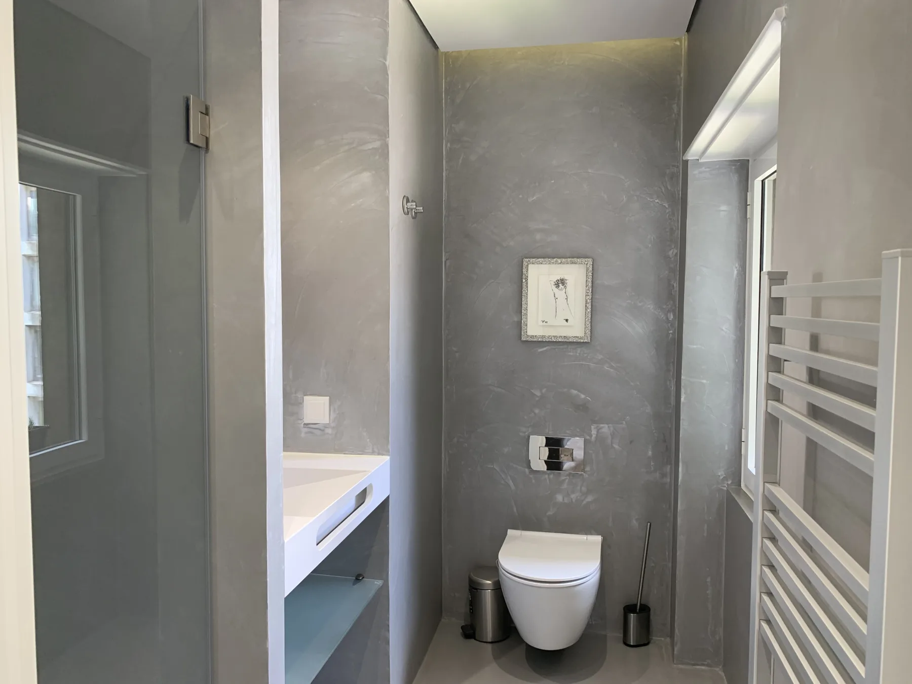 Un baño compacto con un inodoro suspendido y un lavabo estrecho.