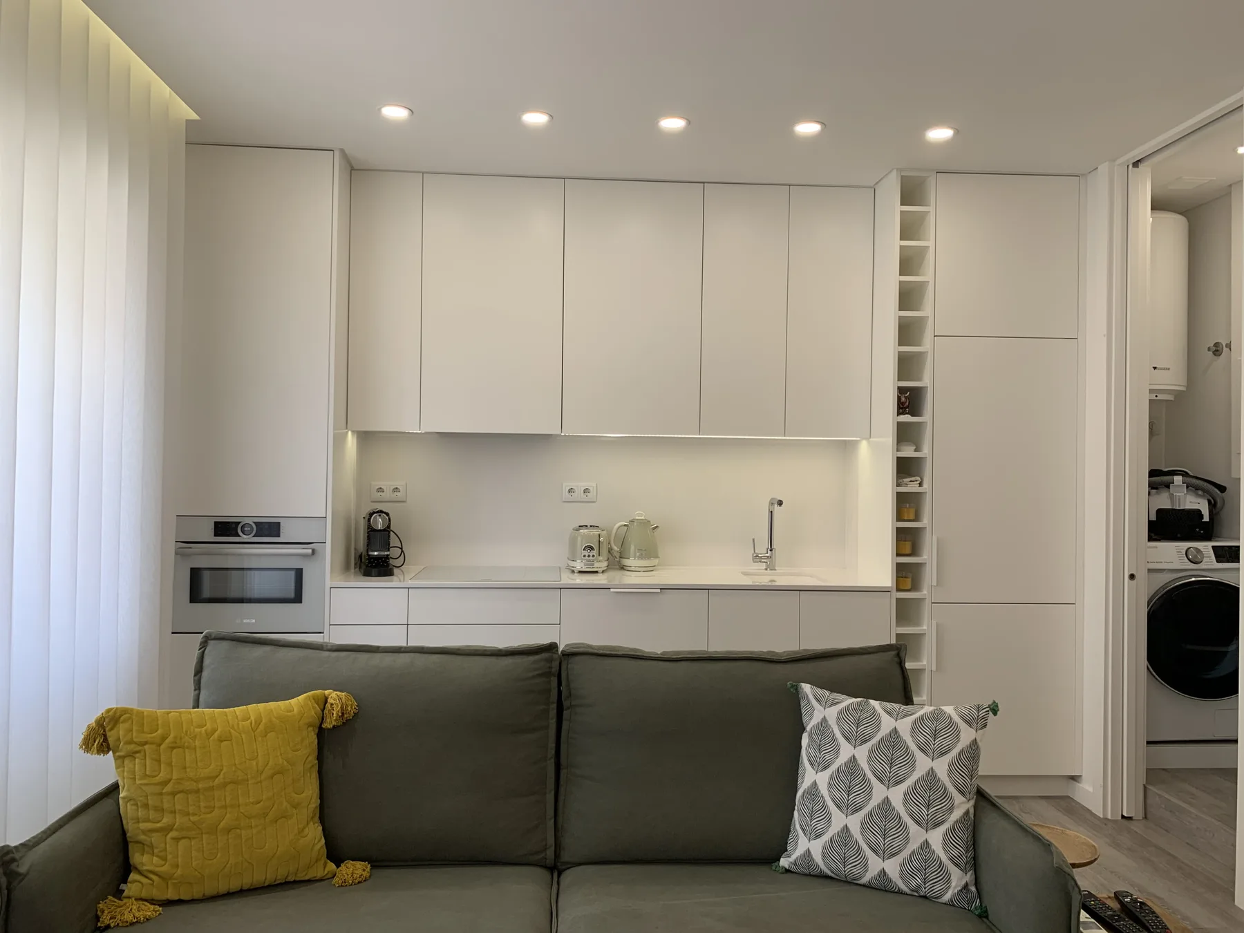 Una cocina moderna con gabinetes blancos y un sofá oscuro en primer plano.