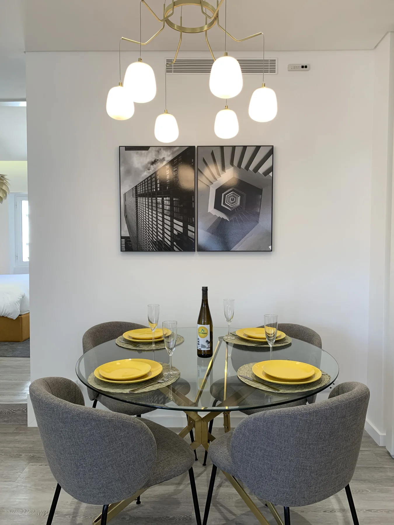 Comedor con mesa de vidrio y asientos tapizados en gris bajo lámparas colgantes.