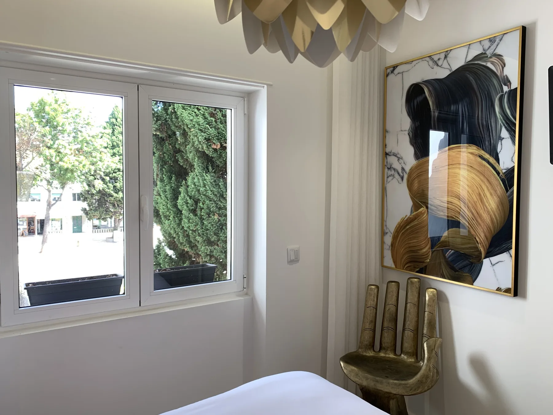 Dormitorio con una ventana, una silla escultórica y una obra enmarcada.