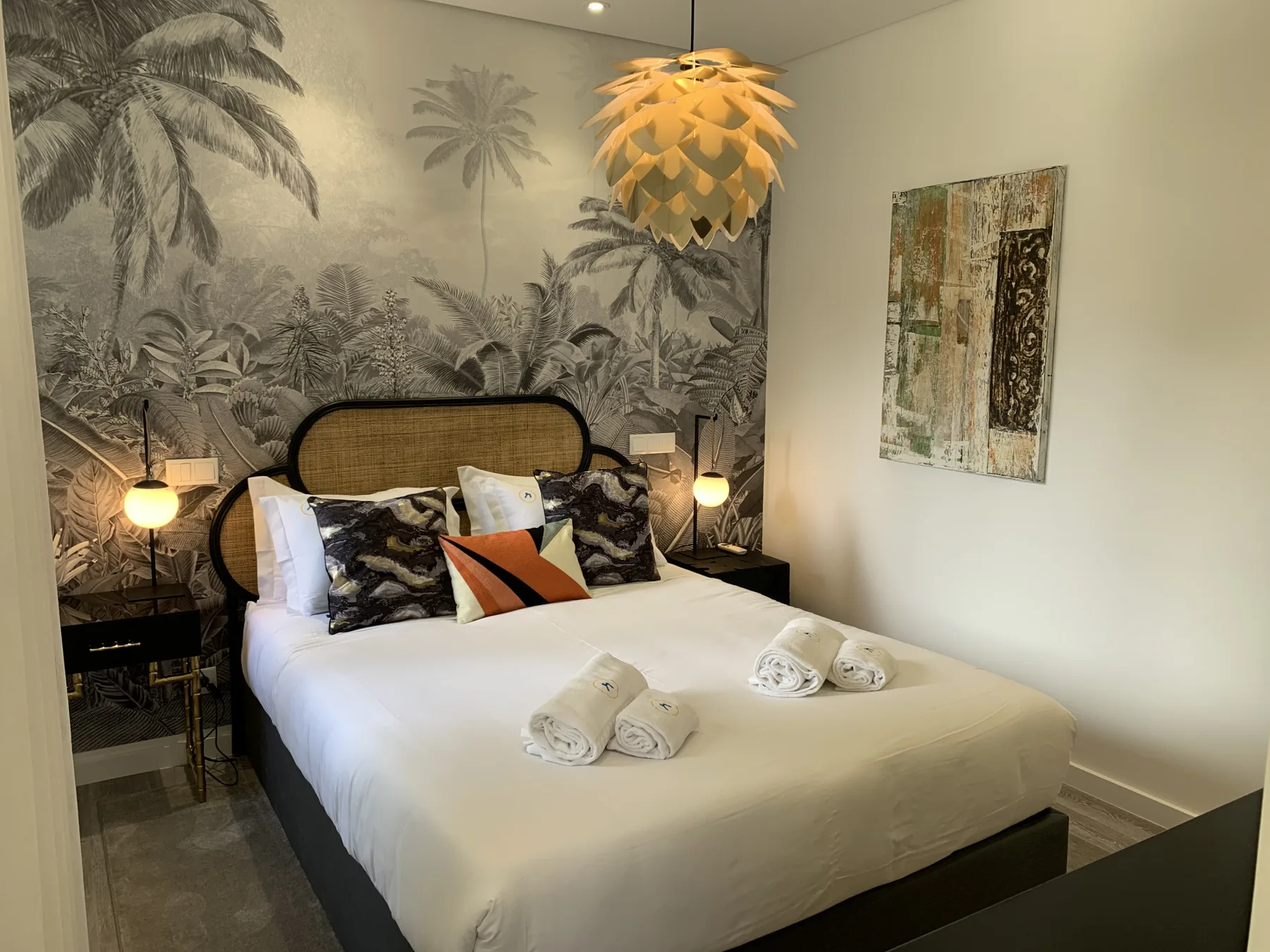 Un dormitorio con una cama bien tendida, almohadas estampadas y un mural tropical.