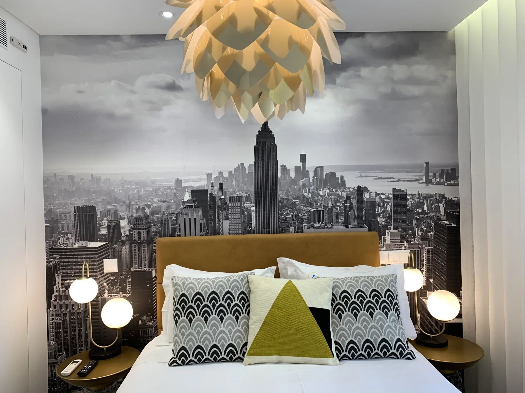 Un dormitorio con cama, cojines estampados y un mural de un horizonte urbano.