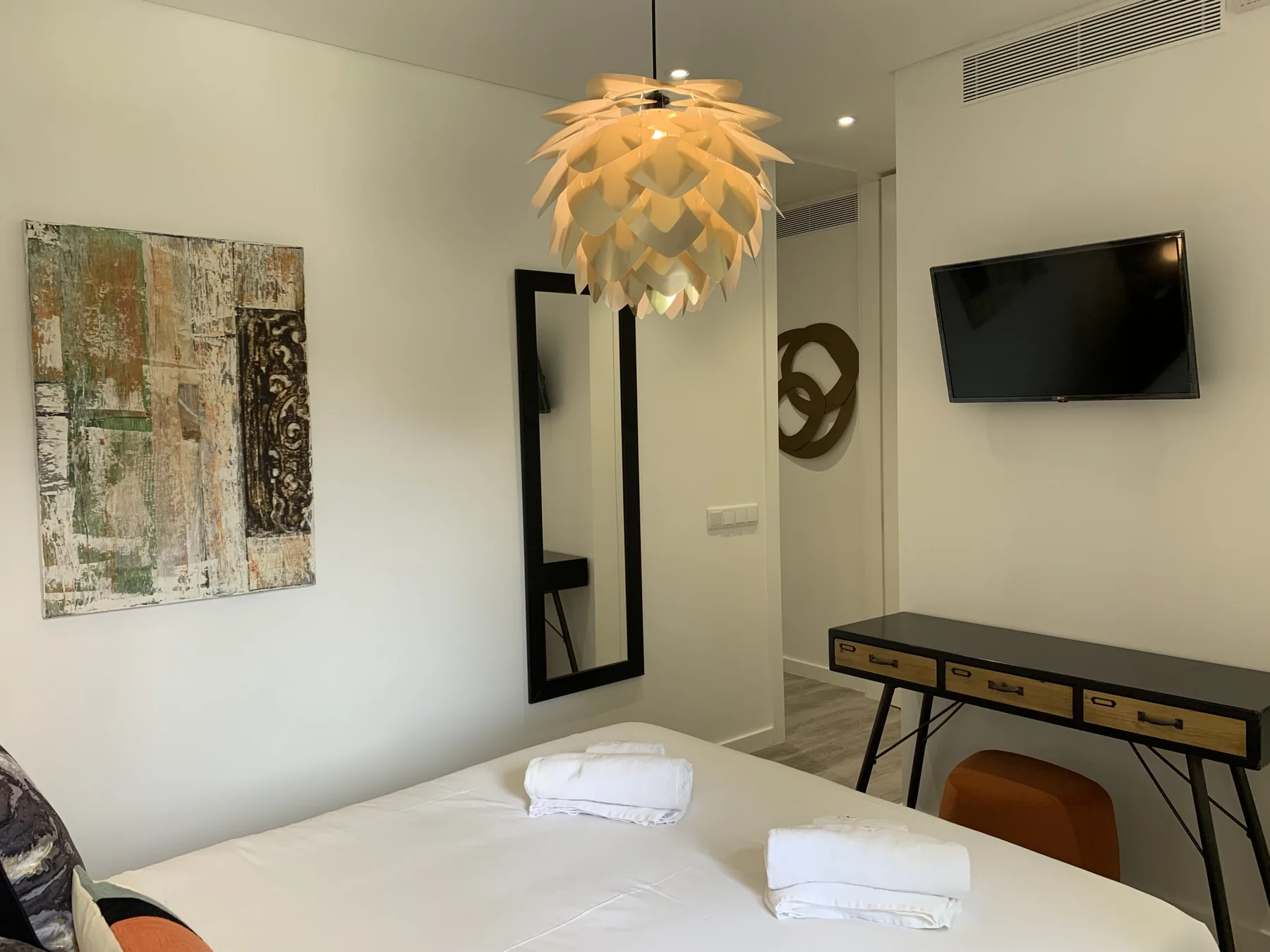 Un dormitorio con un televisor en la pared, arte enmarcado y un escritorio.