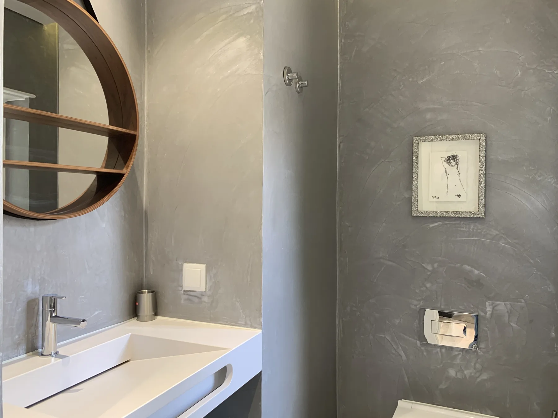 Un tocador de baño con un espejo redondo y paredes grises.