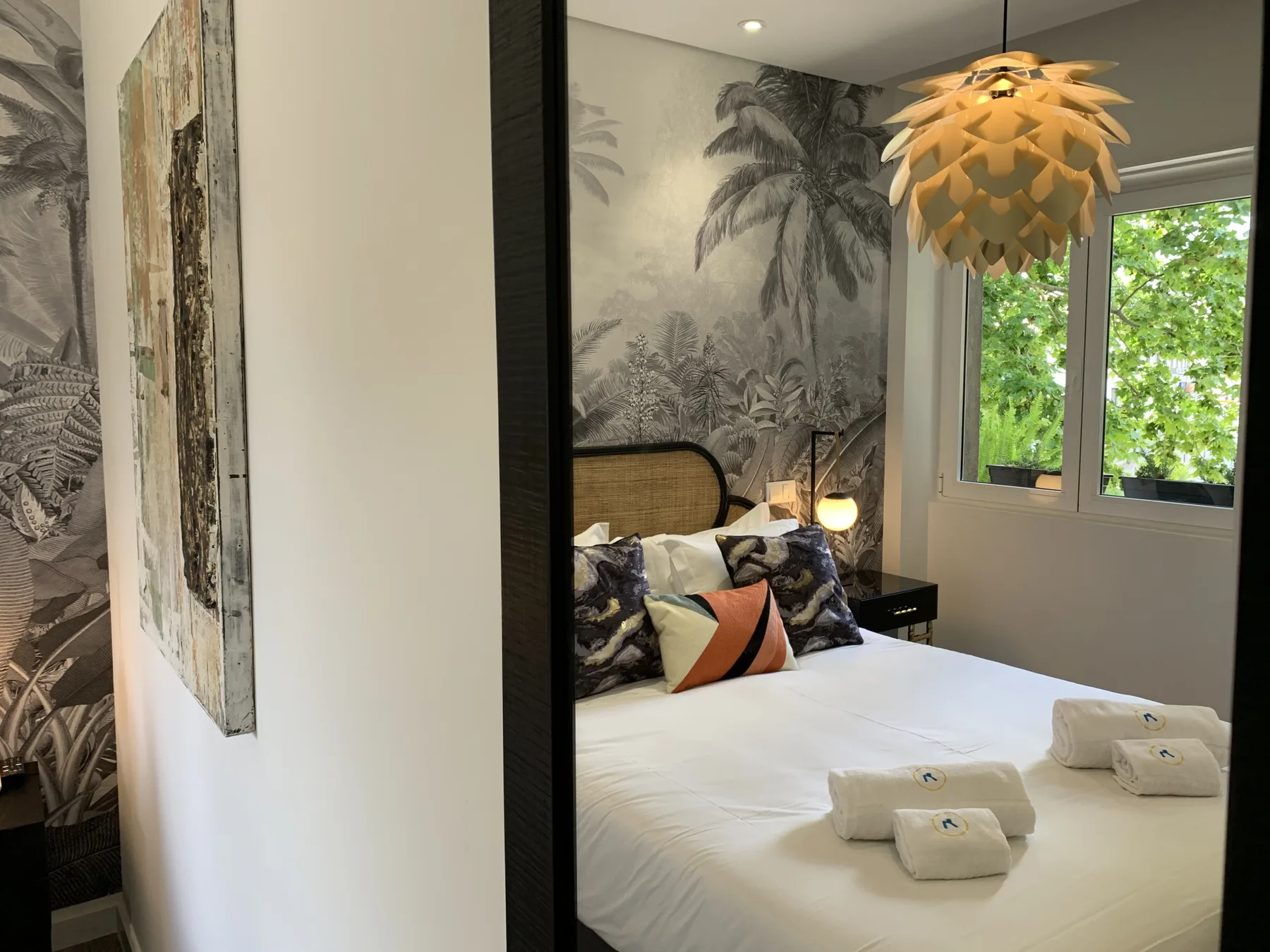 Un dormitorio con una cama blanca y papel pintado de hojas.