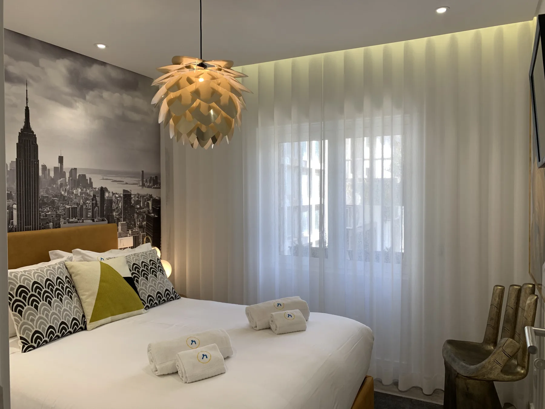 Un dormitorio con una cama bien hecha junto a una gran ventana con cortinas.