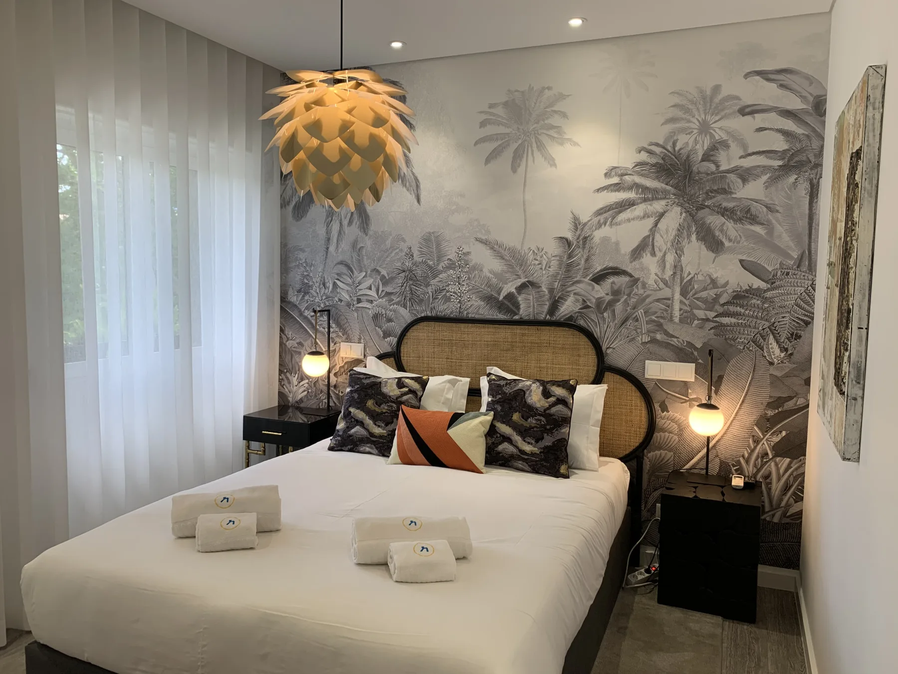 Un dormitorio con una cama, mesitas de noche y un mural de palmeras.