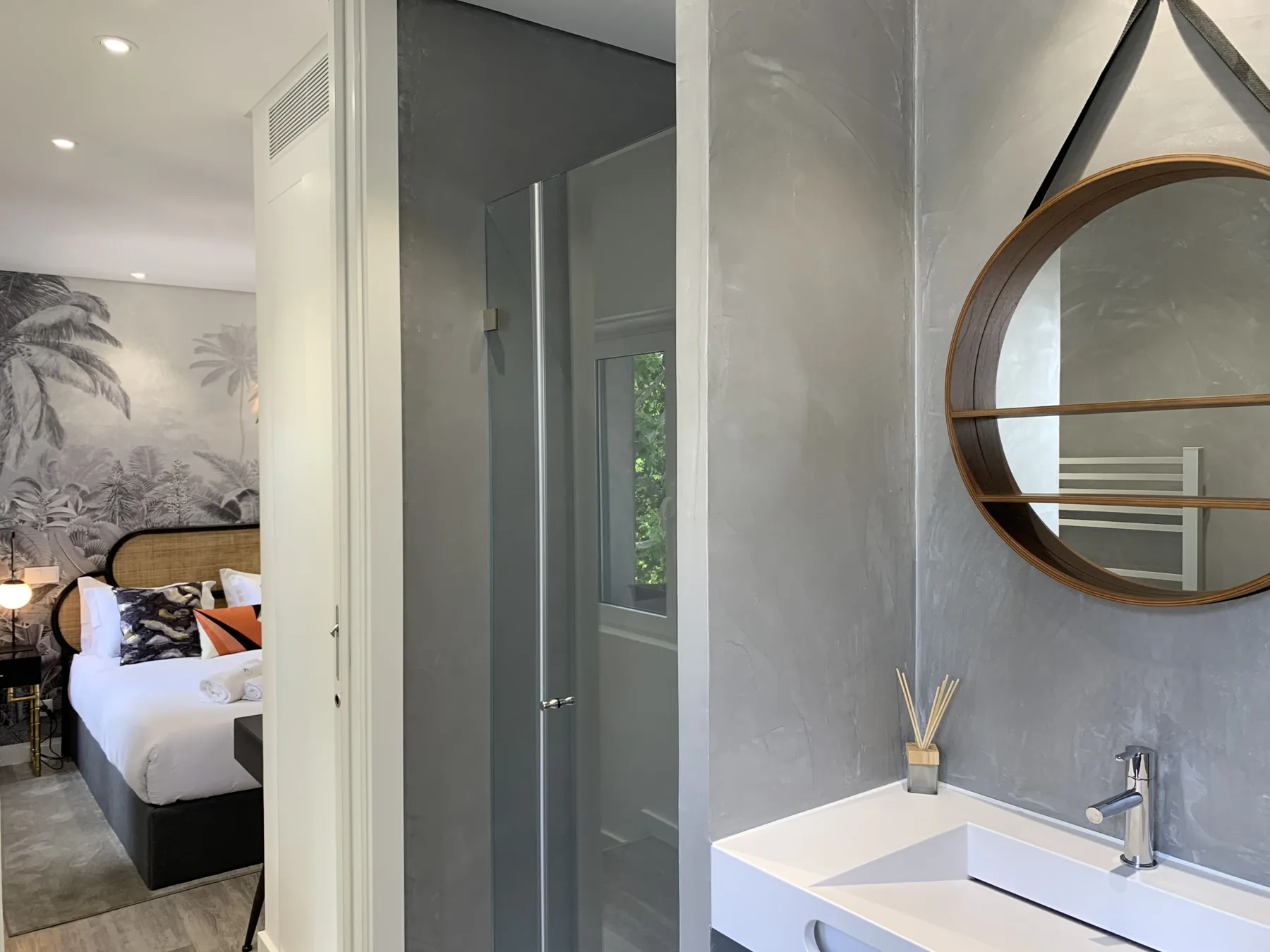 Se ven un dormitorio y un baño a través de una puerta abierta, con una cama y un lavabo.