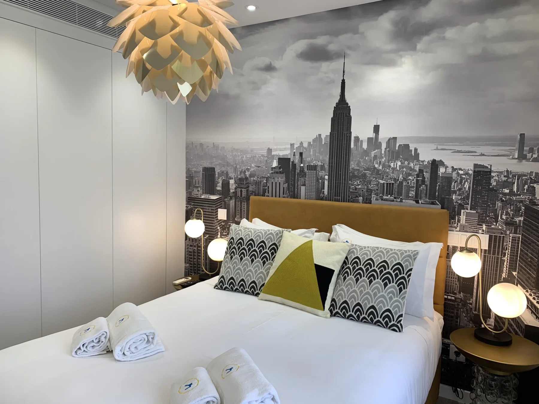 Un dormitorio con una cama bien tendida bajo un mural urbano en blanco y negro.