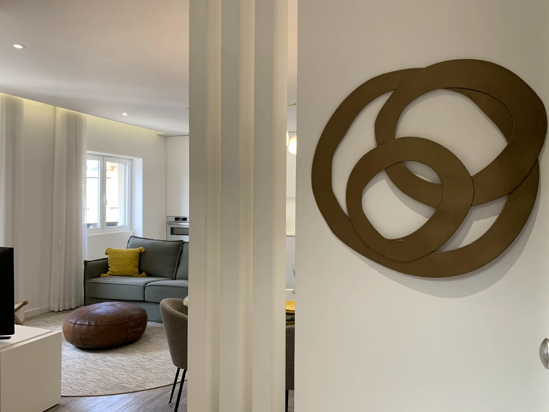 Sala de estar con una zona de asientos gris y una gran escultura circular en la pared.