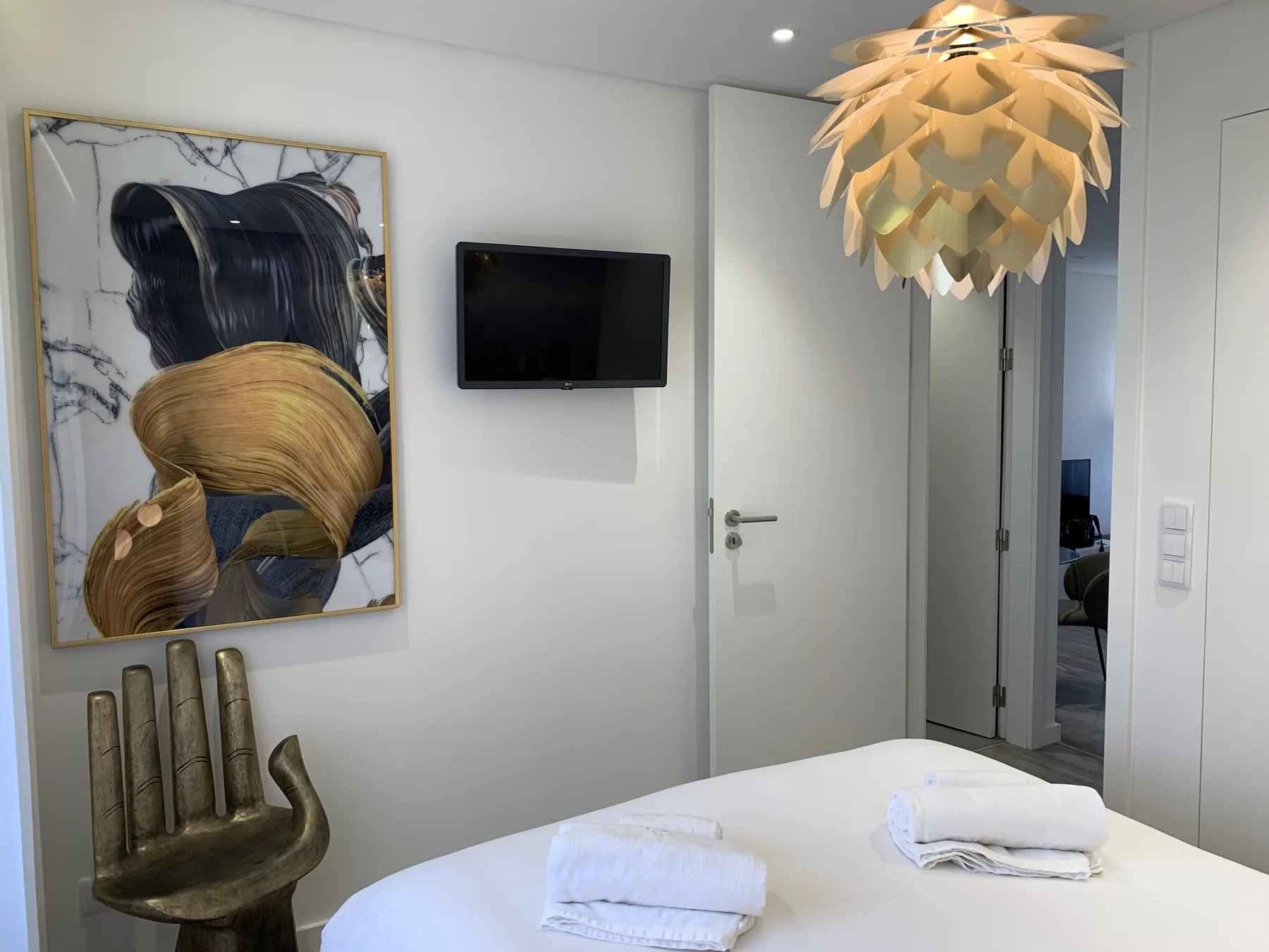 Un dormitorio con una cama bien arreglada, un televisor en la pared y una obra enmarcada.