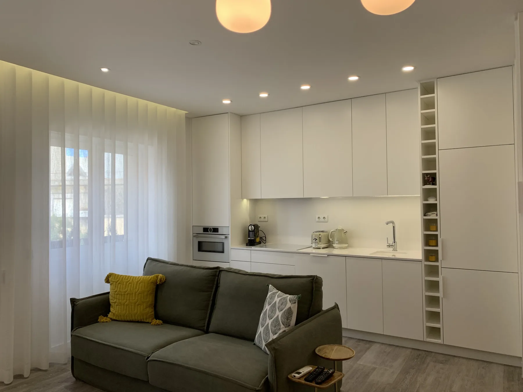 Una zona de estar moderna se abre a una cocina blanca, con asientos en primer plano.
