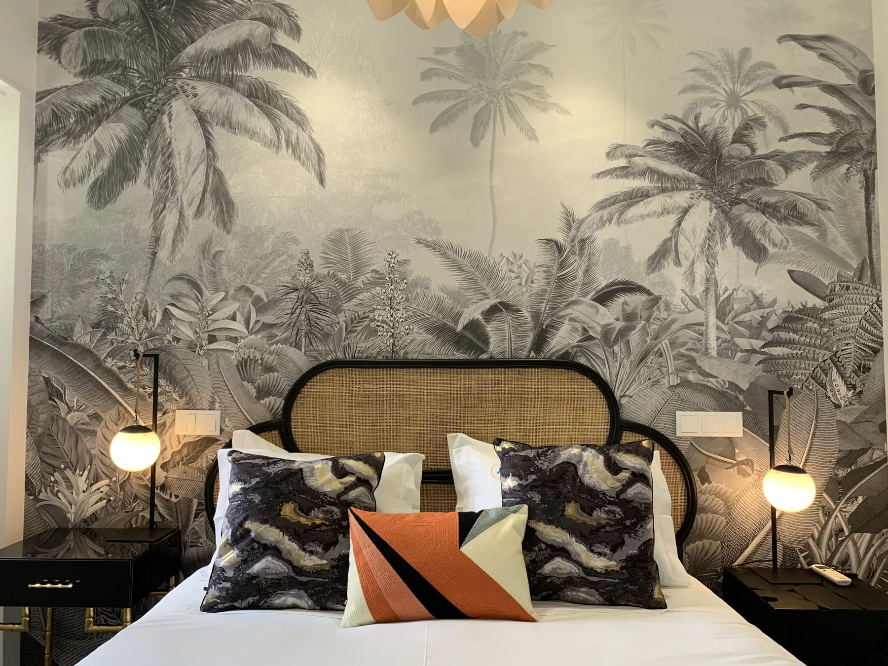 Dormitorio con una cama bien arreglada y un revestimiento mural con palmeras.