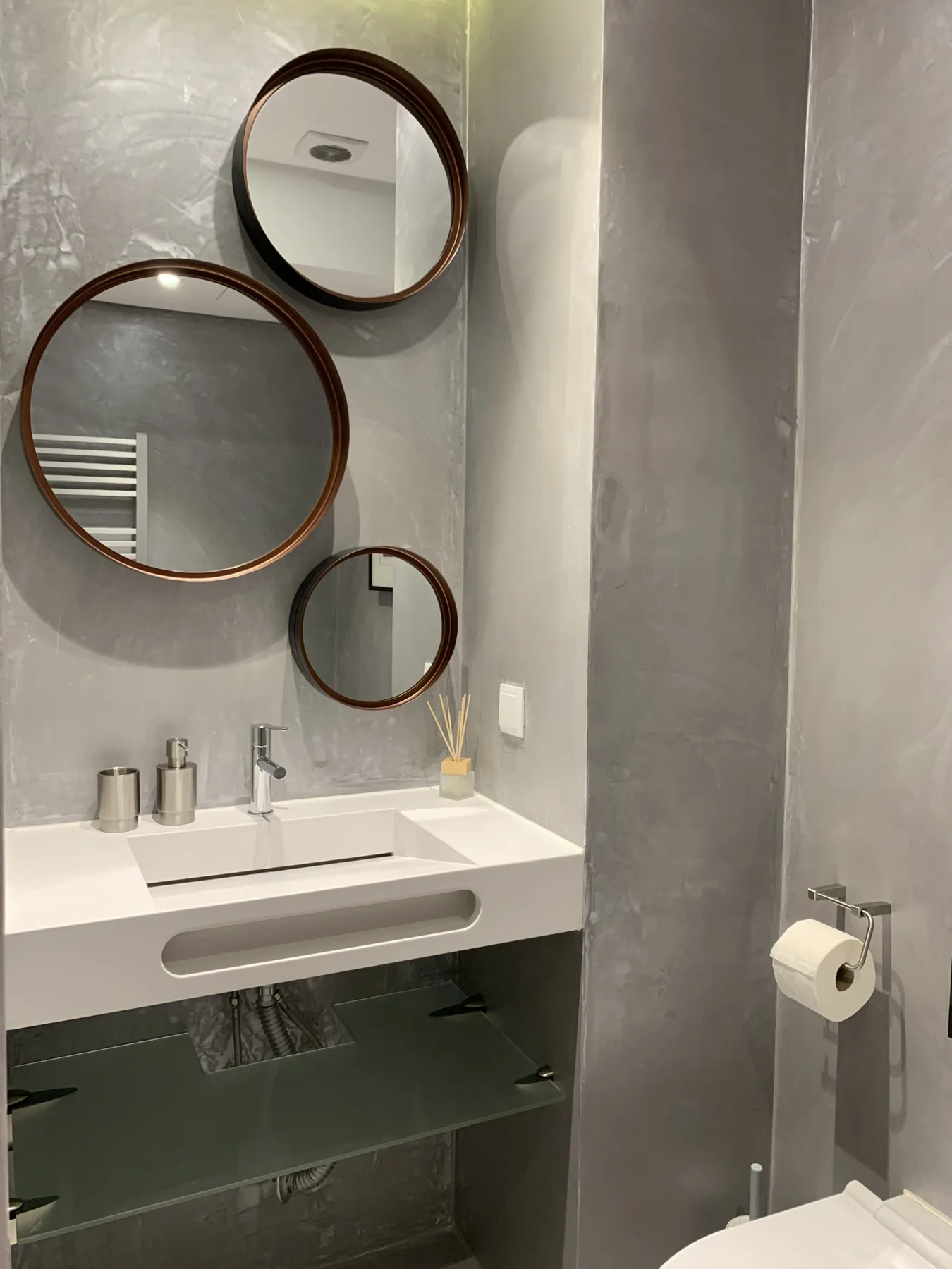 Un lavabo de baño moderno con espejo en la pared y una repisa de vidrio.
